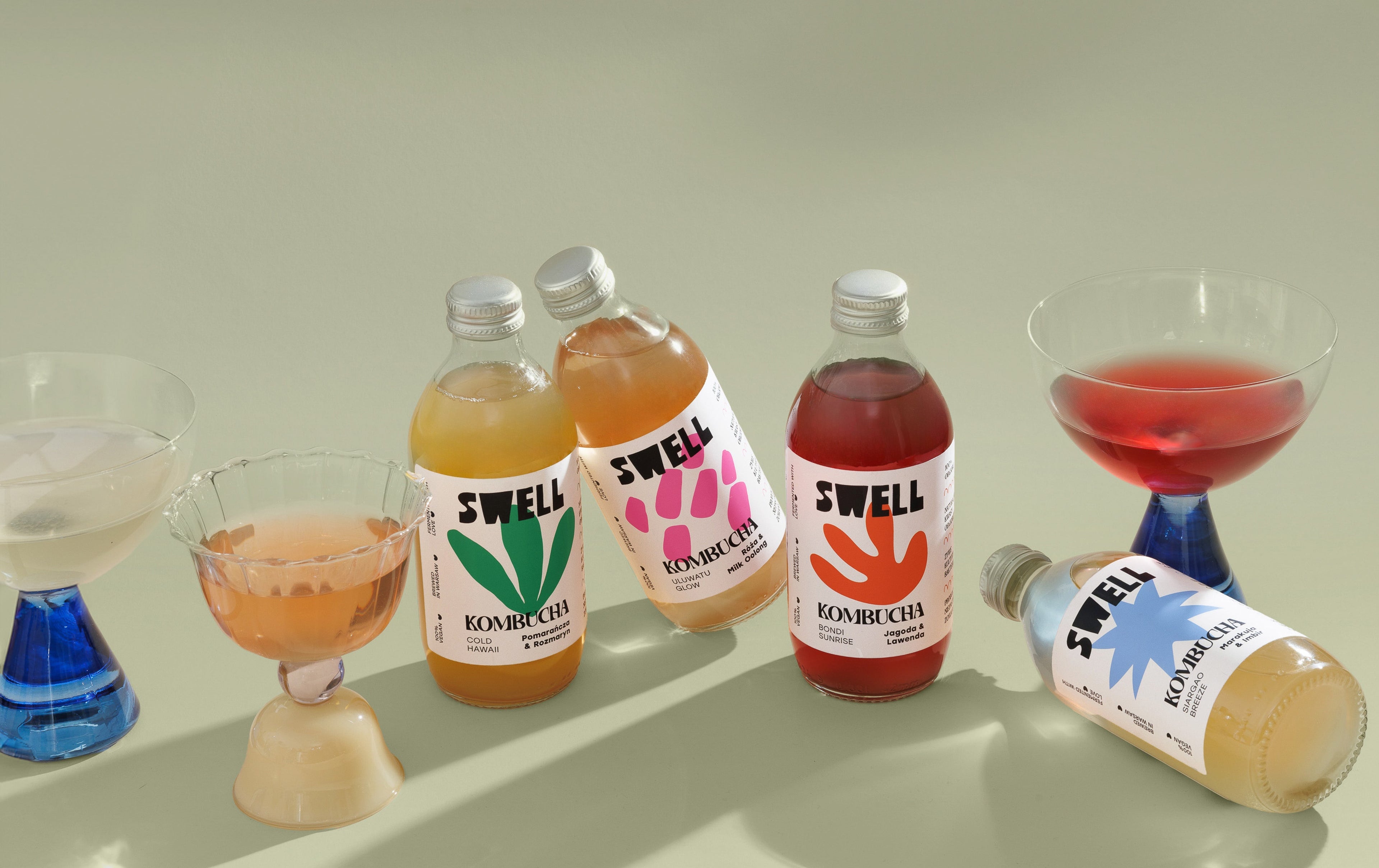Cztery butelki kombuchy mix smaków, trzy kieliszki z nalanymi różnymi smakami